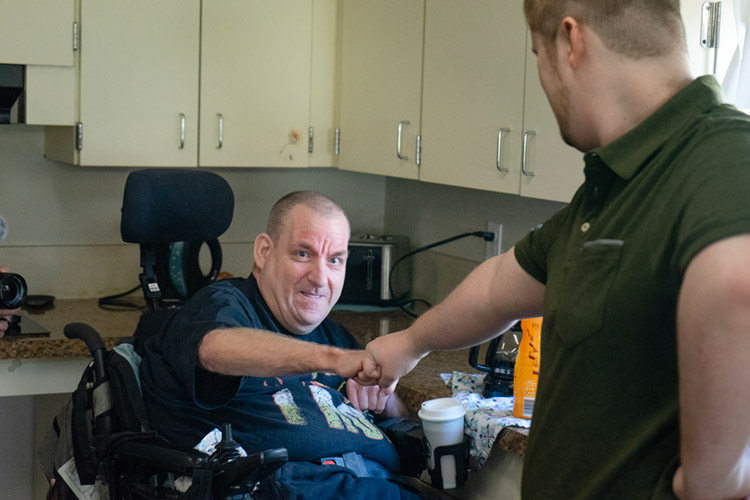 An adult and a support worker sharing a fist bump at home.
