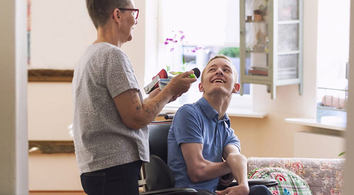 A caregiver sharing a cheerful moment with an adult at home.